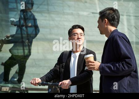 due giovani amici asiatici colleghi che chiacchierano mentre camminano per strada Foto Stock