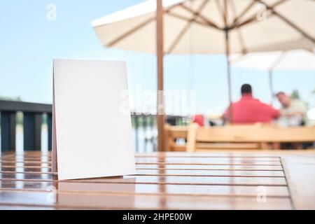 Poster vuoto su un tavolo sulla terrazza di un ristorante, all'aperto, in estate. Spazio vuoto per visualizzare testo, menu, prodotti, promozioni o altre informazioni Foto Stock