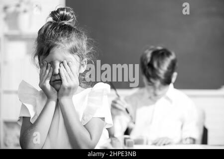 Una ragazza intelligente della scuola grida. Studentessa in uniforme coprendo il suo viso con il braccio piangendo triste di bullismo a scuola in piedi di fronte alla lavagna Foto Stock