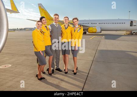 I lavoratori allegri delle compagnie aeree si trovano all'aperto in campo aereo Foto Stock