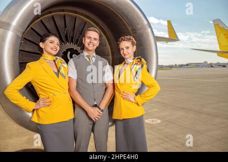I lavoratori allegri della linea aerea in piedi vicino al motore della turbina dell'aeromobile Foto Stock