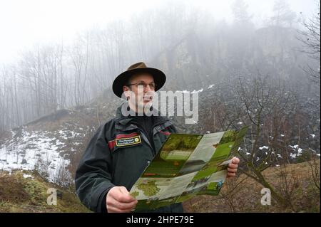 15 febbraio 2022, Hessen, Hoher Meißner: Diethard Lindner del Frau-Holle-Land Geo-Nature Park si trova di fronte al muro di pietra dell'ex miniera a cielo aperto di Kalbe lignite sul versante orientale dell'Hohe Meißner. Un fuoco di giunco è stato bruciante qui per i secoli. A causa di una reazione chimica, la lignite si infiamma da sola e bruciò. In determinate condizioni meteorologiche, l'odore di zolfo può essere percepito a chilometri di distanza. (A dpa 'carbone incandescente nella Hohe Meißner: Fuoco di giunco è stato bruciante per secoli') Foto: Uwe Zucchi/dpa Foto Stock