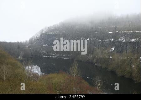 15 febbraio 2022, Hessen, Hoher Meißner: Vista del muro di pietra dell'ex miniera di lignite a pozzo aperto di Kalbe, dietro il lago di Kalbesee, sul versante orientale dell'Hohe Meißner. Un fuoco di giunco è stato bruciante qui per i secoli. Una reazione chimica fa sì che la lignite si infiammare da sola e smolga. In determinate condizioni meteorologiche, l'odore di zolfo può essere percepito a chilometri di distanza. (A dpa 'carbone incandescente nella Hohe Meißner: Fuoco di giunco è stato bruciante per secoli') Foto: Uwe Zucchi/dpa Foto Stock