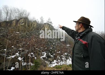 15 febbraio 2022, Hessen, Hoher Meißner: Diethard Lindner del Frau-Holle-Land Geo-Nature Park punta al muro di pietra dell'ex miniera a cielo aperto di Kalbe lignite sul versante orientale dell'Hohe Meißner. Un fuoco di giunco è stato bruciante qui per i secoli. A causa di una reazione chimica, la lignite si infiamma da sola e bruciò. In determinate condizioni meteorologiche, l'odore di zolfo può essere percepito a chilometri di distanza. (A dpa 'carbone incandescente nella Hohe Meißner: Fuoco di giunco è stato bruciante per secoli') Foto: Uwe Zucchi/dpa Foto Stock