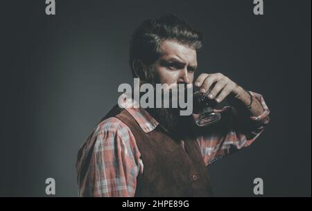 L'uomo con la barba tiene un bicchiere di brandy. Uomo o uomo d'affari beve whiskey su sfondo nero. Foto Stock