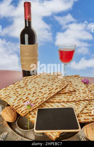 Concetto di festa di Pesach - Vacanza ebraica di Pasqua. Matzah su piatto tradizionale con bottiglia di vino rosso, bicchiere di vino e noci contro il cielo Foto Stock