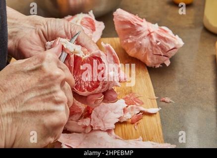 Cook taglia il rosso pomelo all'interno in fette e rimuove la pelle sul tagliere Foto Stock