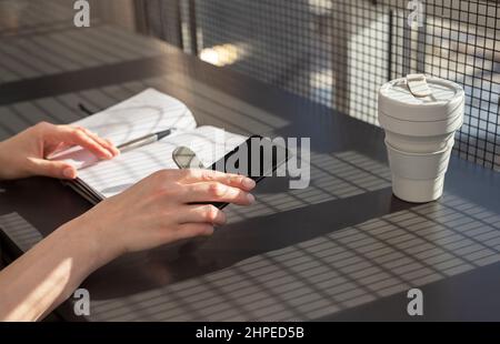 Donna mani che tengono diario. Donna seduta in caffetteria e guardando l'agenda, il programma delle riunioni, le idee scritte in pianificatore. Foto di alta qualità Foto Stock