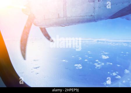 Ala e elica di un piccolo aeroplano durante il volo sopra l'oceano e alcune nuvole, come visto attraverso la finestra della cabina. Foto Stock