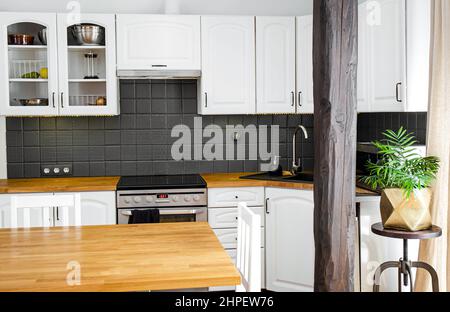 Moderno angolo cottura a casa di colore bianco con piano di lavoro in legno di quercia di colore naturale e vari elettrodomestici. Foto Stock