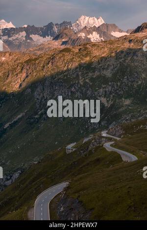 Strada di montagna lastricata vuota che si snoda attraverso il paesaggio. In una piccola sporcizia che si sterrata sul lato della strada è un camper parcheggiato. Il paesaggio è roccioso e con prati, senza alberi. Foto Stock