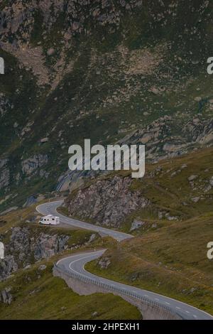 Strada di montagna lastricata vuota che si snoda attraverso il paesaggio. In una piccola sporcizia che si sterrata sul lato della strada è un camper parcheggiato. Il paesaggio è roccioso e con prati, senza la presenza di alberi. Foto Stock