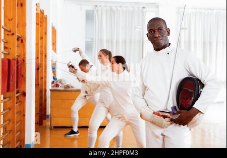 Active americano africano volante maschio in uniforme in piedi con maschera e la lamina a sala di scherma Foto Stock