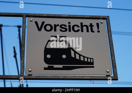 Un cartello sopra un passaggio pedonale avverte dell'avvicinamento dei treni. Foto Stock