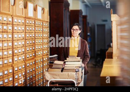 Ritratto di donna bibliotecaria dai toni caldi con libri all'interno della biblioteca, spazio copia Foto Stock