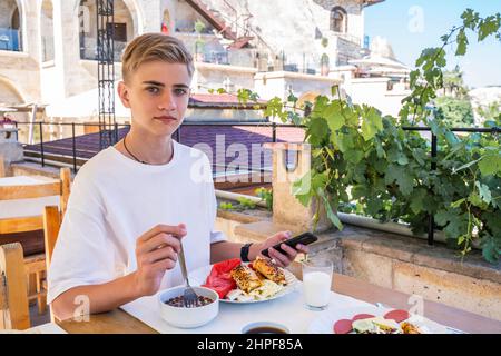 L'adolescente mangia una colazione tradizionale turca su un tetto che si affaccia sulla città di Goreme in Cappadocia. Foto Stock