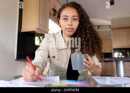 Ritratto di fidato biraciale femminile freelance che tiene la tazza di lavoro a casa ufficio Foto Stock