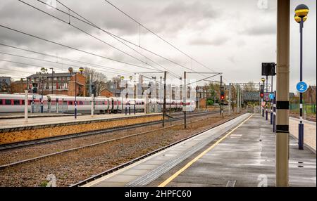 La fine di una piattaforma ferroviaria dove un treno lascia una stazione ferroviaria. Ci sono luci di segnalazione sulle piattaforme e un cielo con le nuvole è sopra. Foto Stock