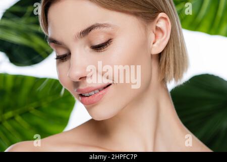 primo piano di una giovane donna felice con pelle perfetta vicino a foglie di palma verde su bianco Foto Stock