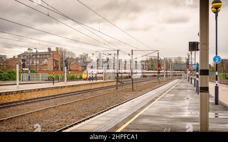 La fine di una piattaforma ferroviaria dove un treno lascia una stazione ferroviaria. Ci sono luci di segnalazione sulle piattaforme e un cielo con le nuvole è sopra. Foto Stock