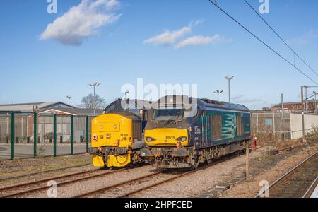 Due locomotive diesel sono parcheggiate in un fianco accanto ad una recinzione. Ci sono cavi e un cielo limpido con nuvola di luce sopra. Foto Stock