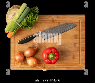 Coltello con disegno saldato e alcune verdure sul pannello di taglio in legno di bambù nella parte posteriore nera Foto Stock