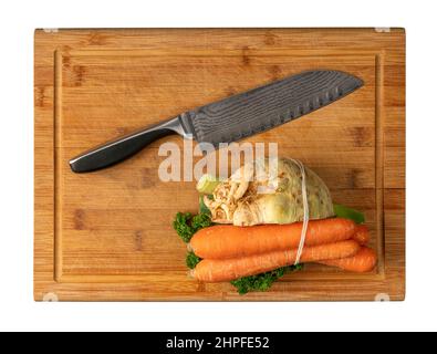 Coltello con disegno saldato e un mazzo di verdure sul tagliere in legno di bambù nella parte posteriore bianca Foto Stock