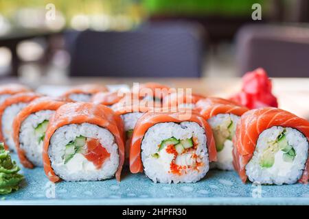 Il sushi roll Philadelphia con salmone, anguilla affumicata, avocado, formaggio cremoso su piatto blu nel caffè. Menu di sushi. Cucina giapponese Foto Stock