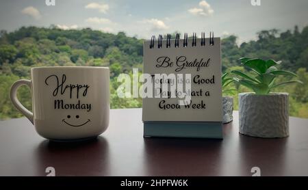 Primo piano del testo di saluto mattina sulla tazza di caffè e citazione sul blocco note - Lunedi felice e oggi è un buon giorno per iniziare una buona settimana. Con piante e. Foto Stock