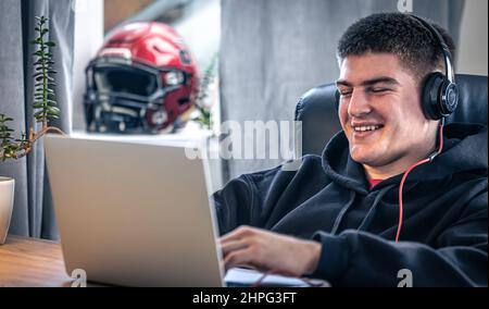 Un giovane atleta maschio si siede di fronte a un computer portatile nella sua stanza. Foto Stock