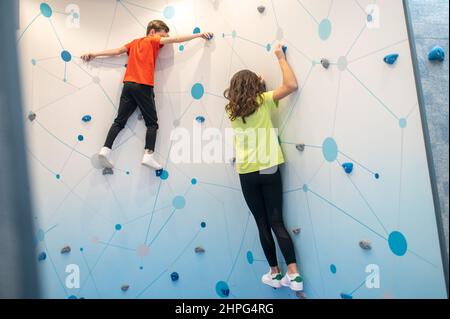Vista posteriore dei bambini appesi alla parete di pratica di arrampicata Foto Stock