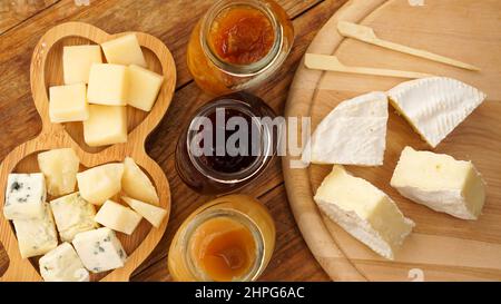 Vasetti di marmellate fatte in casa e miele e una varietà di formaggi su un tavolo di legno. Piatto di formaggi per antipasti con spiedini di legno per cibo. Vista dall'alto Foto Stock