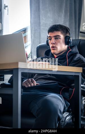 Un giovane atleta maschio si siede di fronte a un computer portatile nella sua stanza. Foto Stock