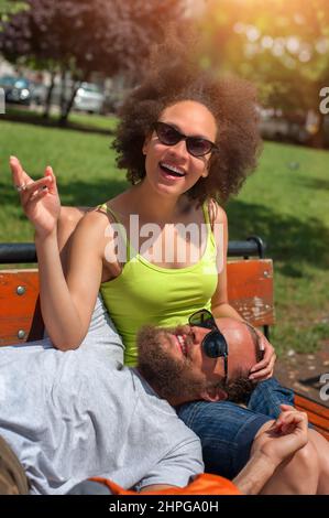 Bella coppia giovane che riposa insieme su una panca di legno nel parco Foto Stock