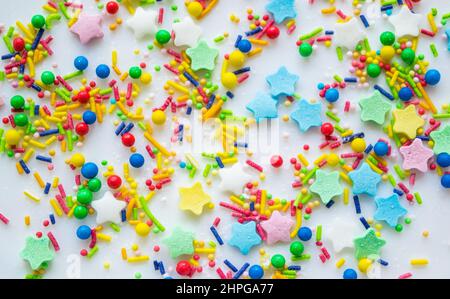 Sfondo festivo multicolore di una dispersione di caramelle spolverate di zucchero per cupcakes e altri dolci in forma di stelle, bastoni e palle. Spazio di copia Foto Stock