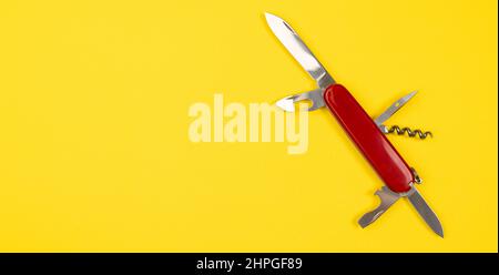 Jack di tutti i mestieri concetto con l'esercito svizzero multi tolls coltello tasca isolato su sfondo giallo. Coltello militare rosso con spazio per la copia Foto Stock