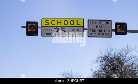 Segnaletica stradale con avvertimento per il limite di velocità della scuola di 25 mph. Uso del telefono cellulare vietato durante la guida, prevenzione degli incidenti nella zona della scuola. Foto Stock