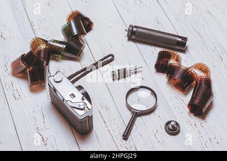 Vecchia telecamera retrò, film e altri accessori su un tavolo bianco. Sfondo in legno Foto Stock