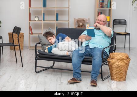 Papà legge un libro e il figlio si addormenta mentre legge. Foto Stock