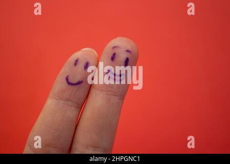 Volti sorridenti disegnati su dita isolate su sfondo rosso. Concetto di felicità e amicizia. Foto Stock