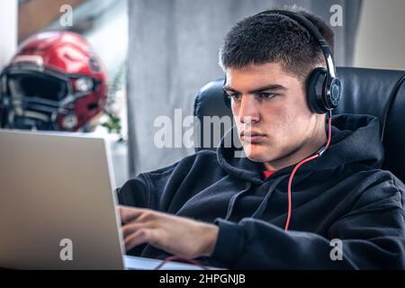 Un giovane atleta maschio si siede di fronte a un computer portatile nella sua stanza. Foto Stock