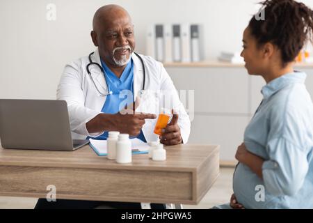 Gravidanza, Ostetricia, Ginecologia, Medicina, Sanità e concetto di persone. Ginecologo maschio nero che dà pillole a sorridente donna incinta durante appo Foto Stock