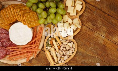 Diversi gustosi antipasti su sfondo di legno, vista dall'alto. Spuntini per vino. Piatto di formaggi e carni. Salsicce, formaggi, noci, uva, cracker Foto Stock
