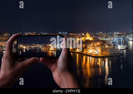 Turista fotografa tre città di Malta di notte. Foto scattata da la Valletta. Il Grand Harbour illuminato di notte. Foto Stock