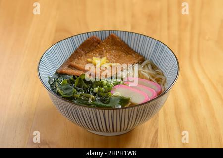 Cucina giapponese fritto, kitsune di noodle di udon soba in una ciotola isolata su tavolo di legno vista dall'alto Foto Stock
