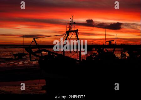 Silhouette di un peschereccio da traino sull'estuario del Tamigi a Leigh-on-Sea Essex con un luminoso tramonto arancione a bassa marea Foto Stock