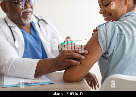 Donna nera che riceve l'iniezione di vaccino di Coronavirus seduta con il Dottore Indoor Foto Stock