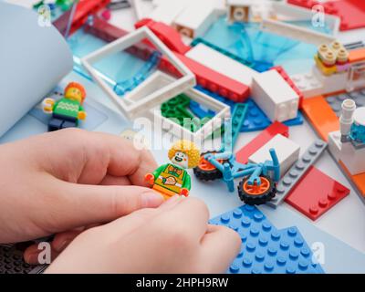 Tambov, Federazione Russa - 09 febbraio 2022 Un bambino che tiene una minifcifra di lego clown mentre costruisce un insieme di Lego. Primo piano. Foto Stock