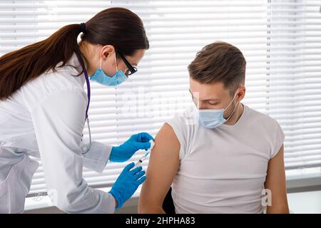 Il medico tiene una siringa prima di fare un'iniezione a un paziente in una maschera medica. Covid-19 o vaccino contro il coronavirus. Vaccinazione della popolazione Foto Stock
