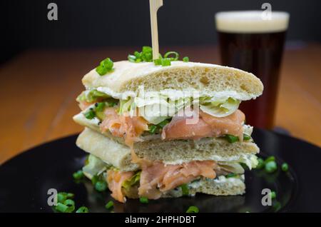 Delizioso sandwich al salmone da vicino e bicchiere di birra. Foto Stock